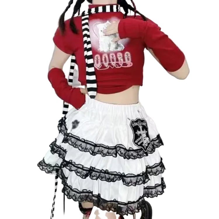A person wearing a red cropped short-sleeve top with a white cat graphic and black-and-white striped tie detail, paired with a white tiered skirt featuring black lace trim and a black skull patch.