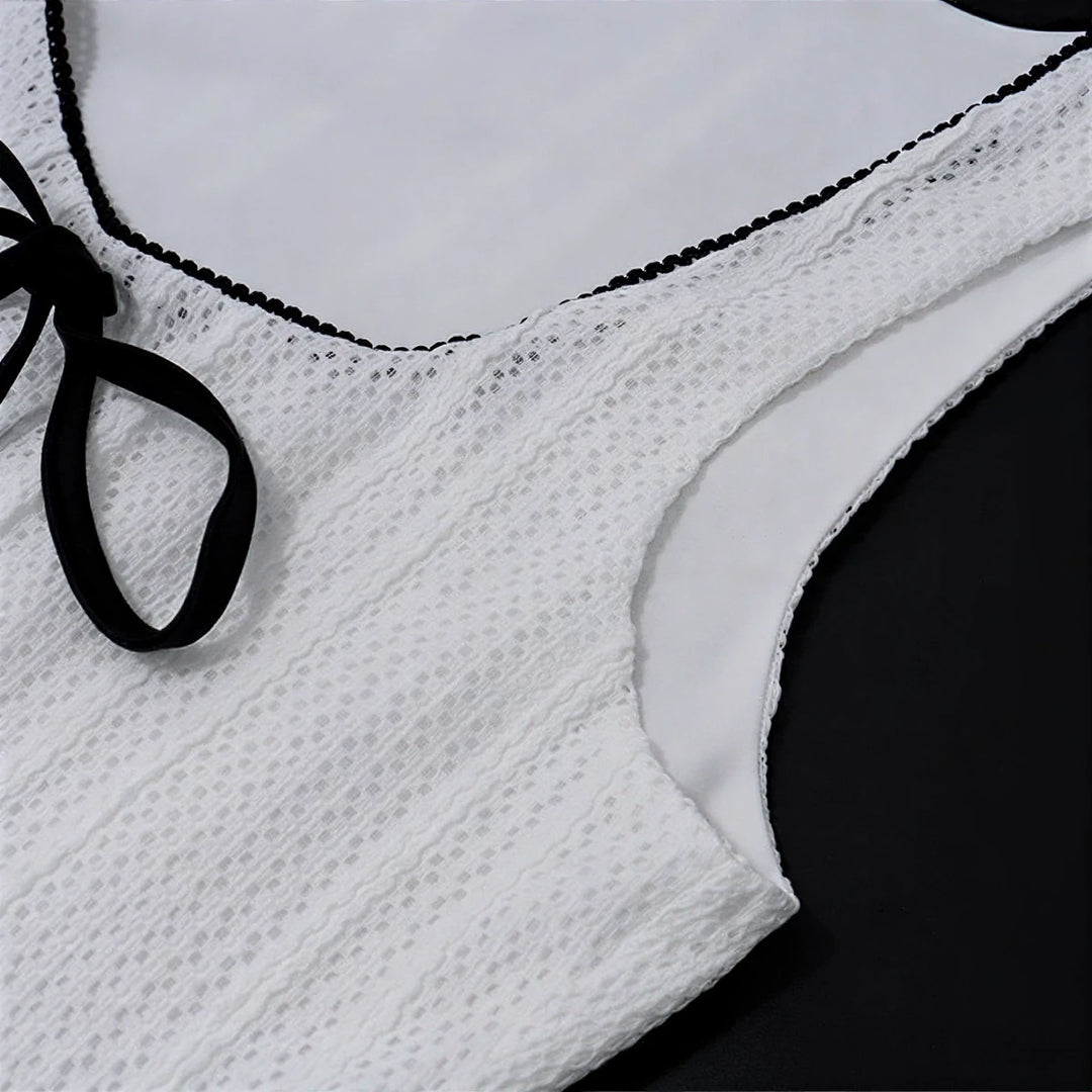 White lace dress with black trim and tie detail at neckline.