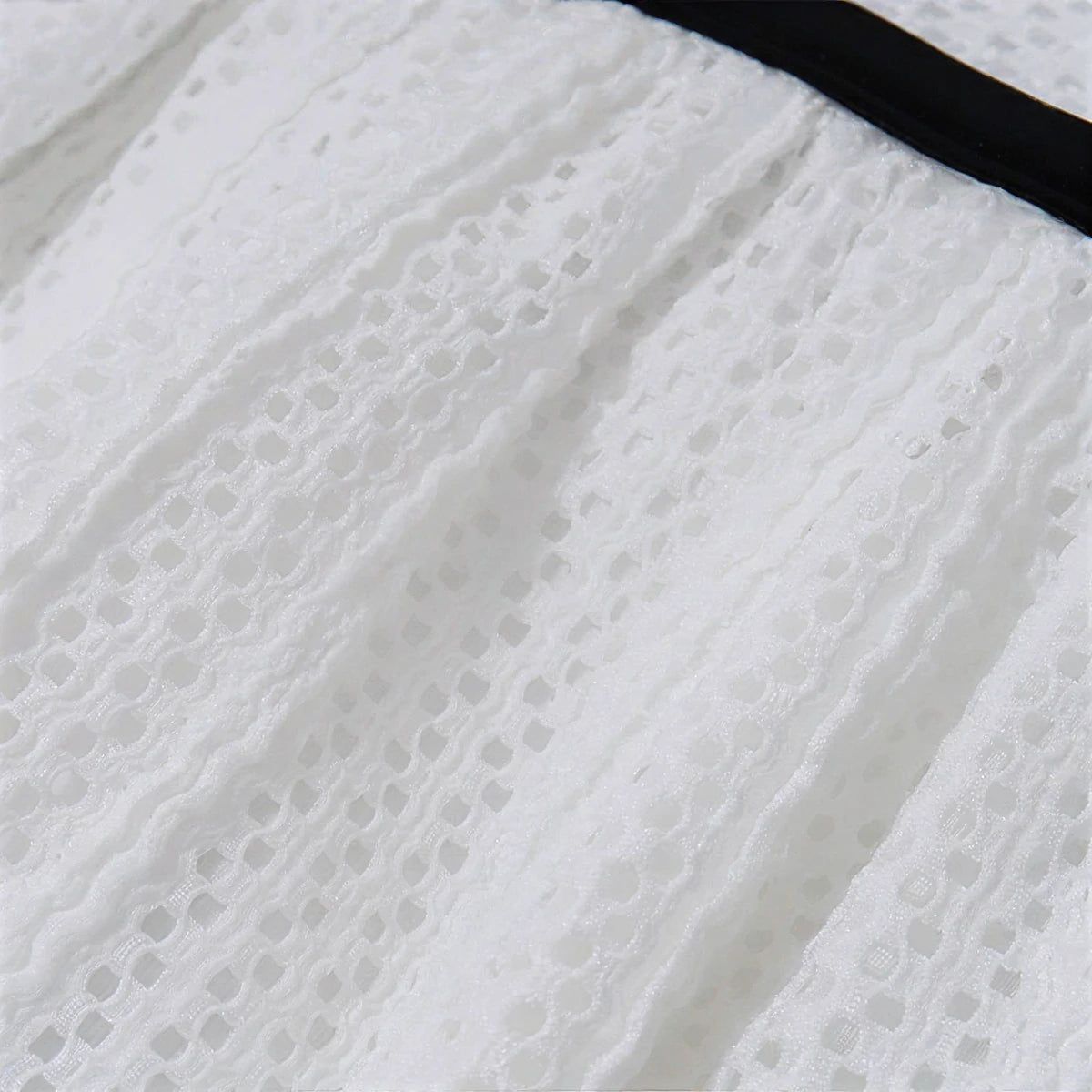 White lace dress with black trim, delicate eyelet pattern, soft textured fabric.