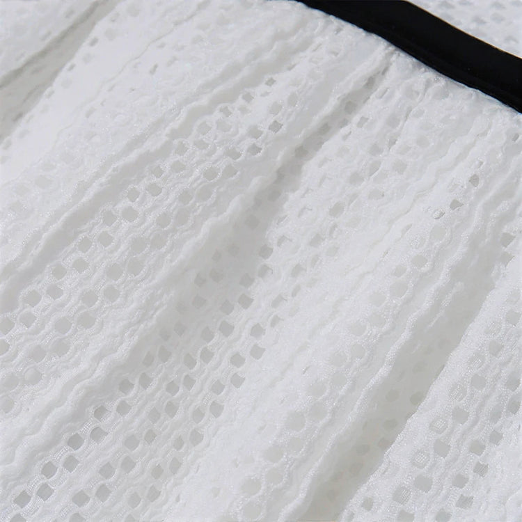 White lace dress with black trim, delicate eyelet pattern, soft textured fabric.