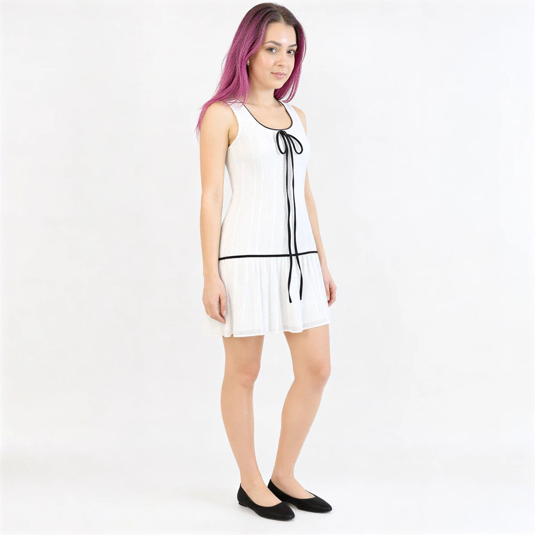 White pleated sleeveless dress with black trim and tie detail.